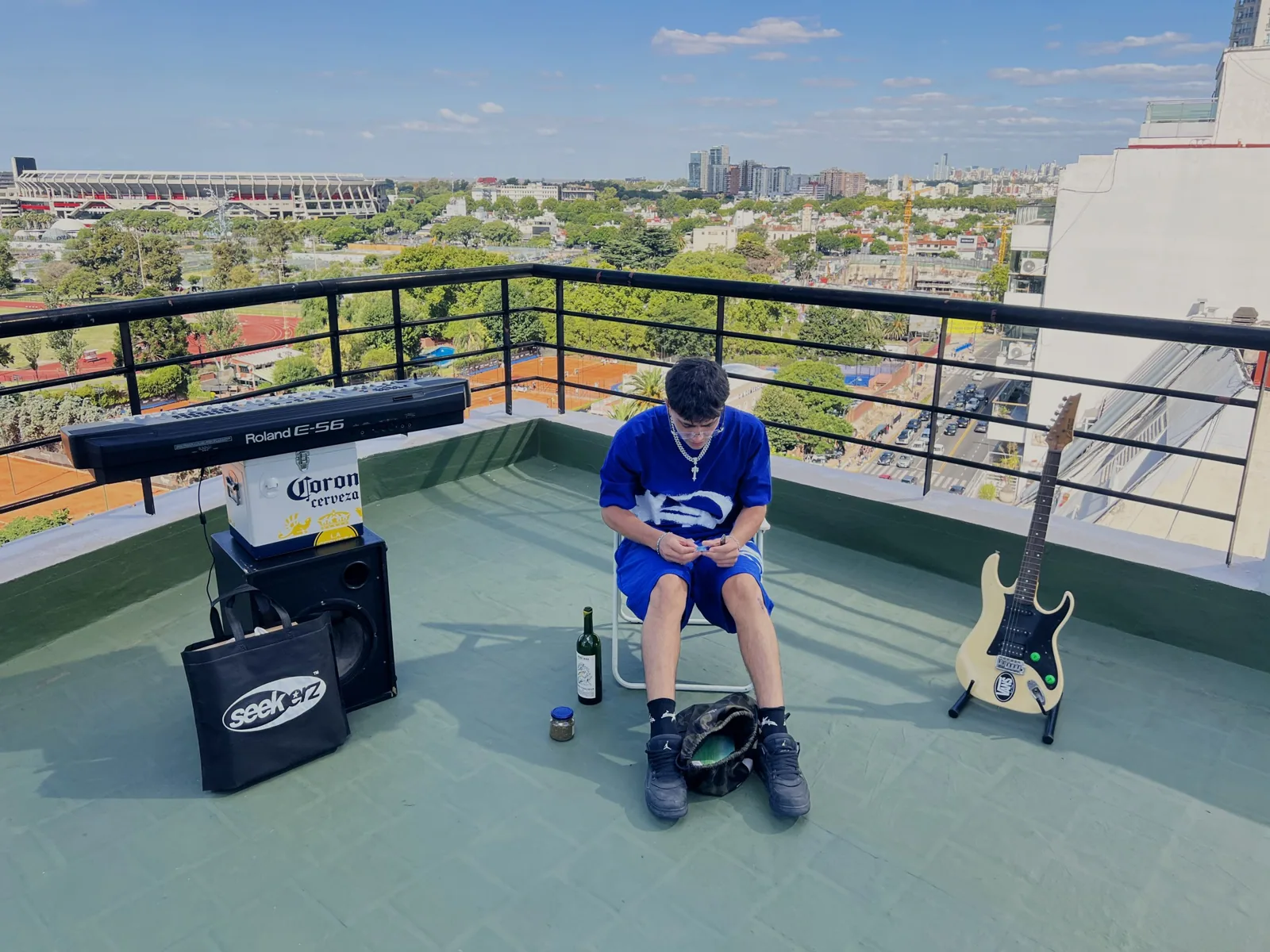 Un integrante del equipo sentado en una terraza de Buenos Aires, con el estadio y la ciudad de fondo, un teclado y una guitarra alrededor
